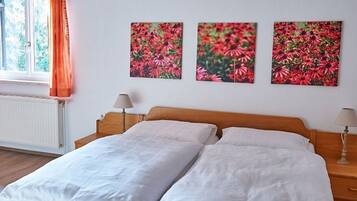 Une chambre à coucher avec un lit en bois, une literie blanche, deux lampes de chevet et trois tableaux représentant des fleurs, accrochés au mur.