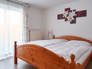 Un lit en bois dans une pièce équipée d’un radiateur, d’une lampe et d’une fenêtre avec des rideaux.