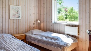 Ein Zimmer mit zwei Betten, einem Nachttisch, einer Wandlampe und einem Fenster mit Blick ins Grüne.