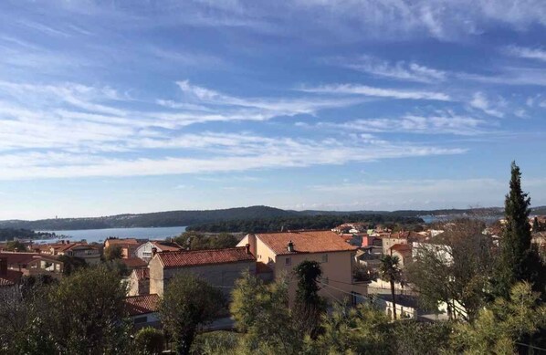 A coastal town with terracotta-roofed buildings, a body of water, and a hilly landscape in the distance. - Holiday apartment with air conditioning (Medulin)