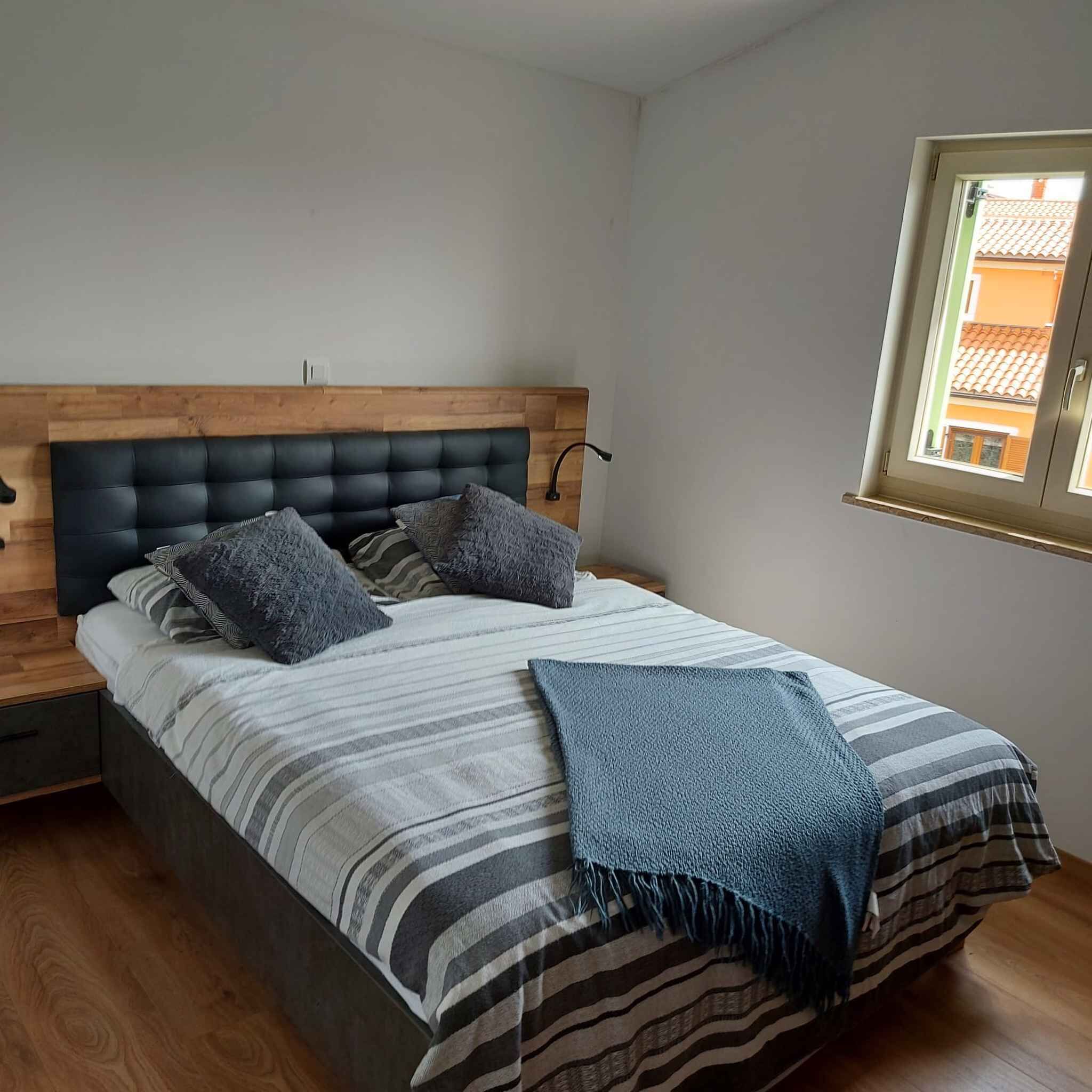 A bedroom with a bed, wooden headboard, and a window with a view of buildings.