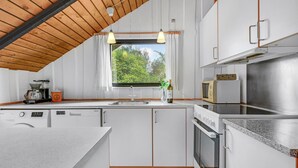 Eine moderne Küche mit weißen Schränken, einer Holzbalkendecke und einem Fenster mit Blick auf Grünflächen.