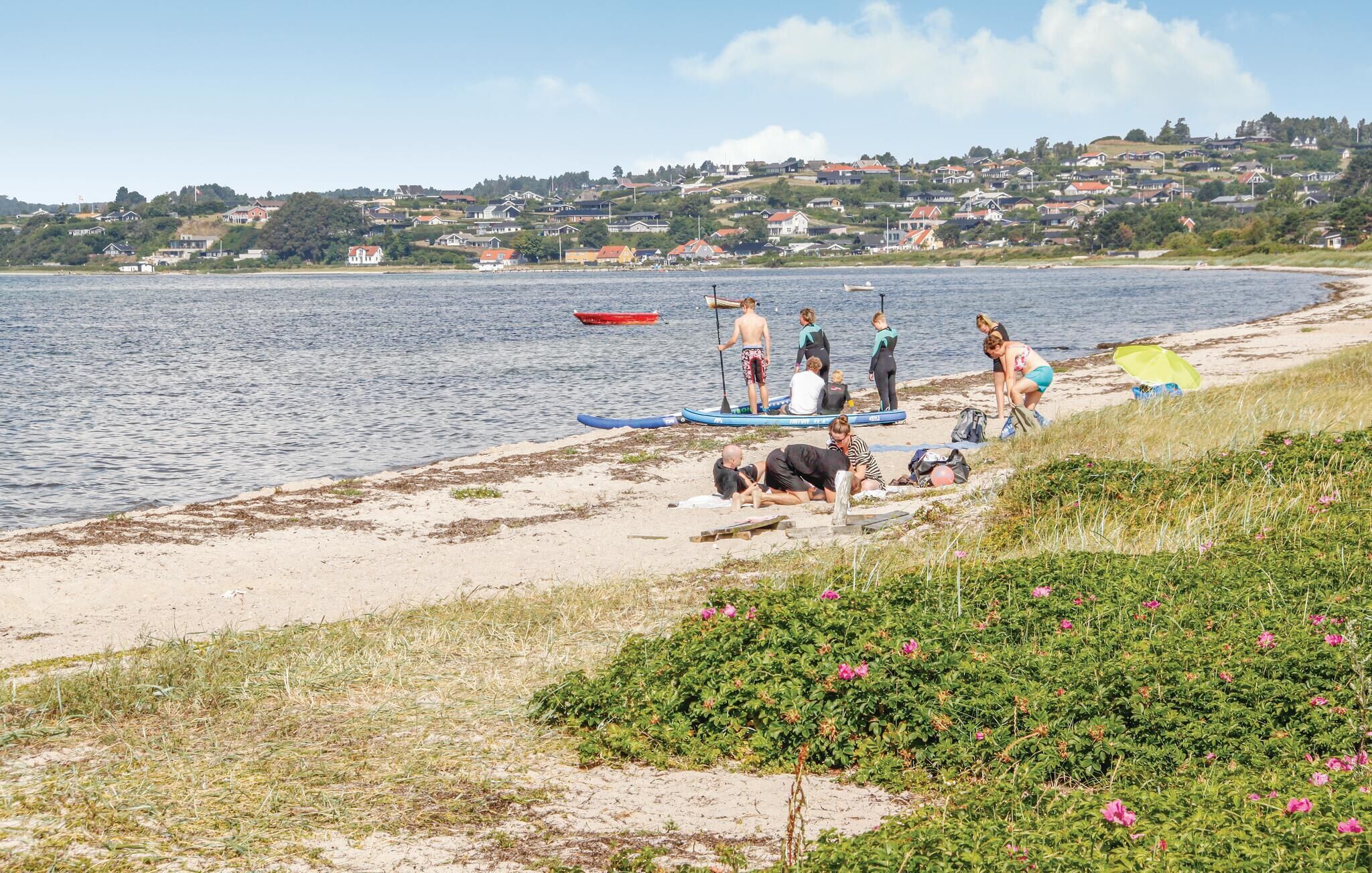 A beach with people preparing for water activities, a red boat, and houses in the background.