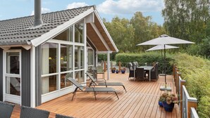Une maison moderne dotée d’une terrasse en bois, de grandes fenêtres et de mobilier d’extérieur.