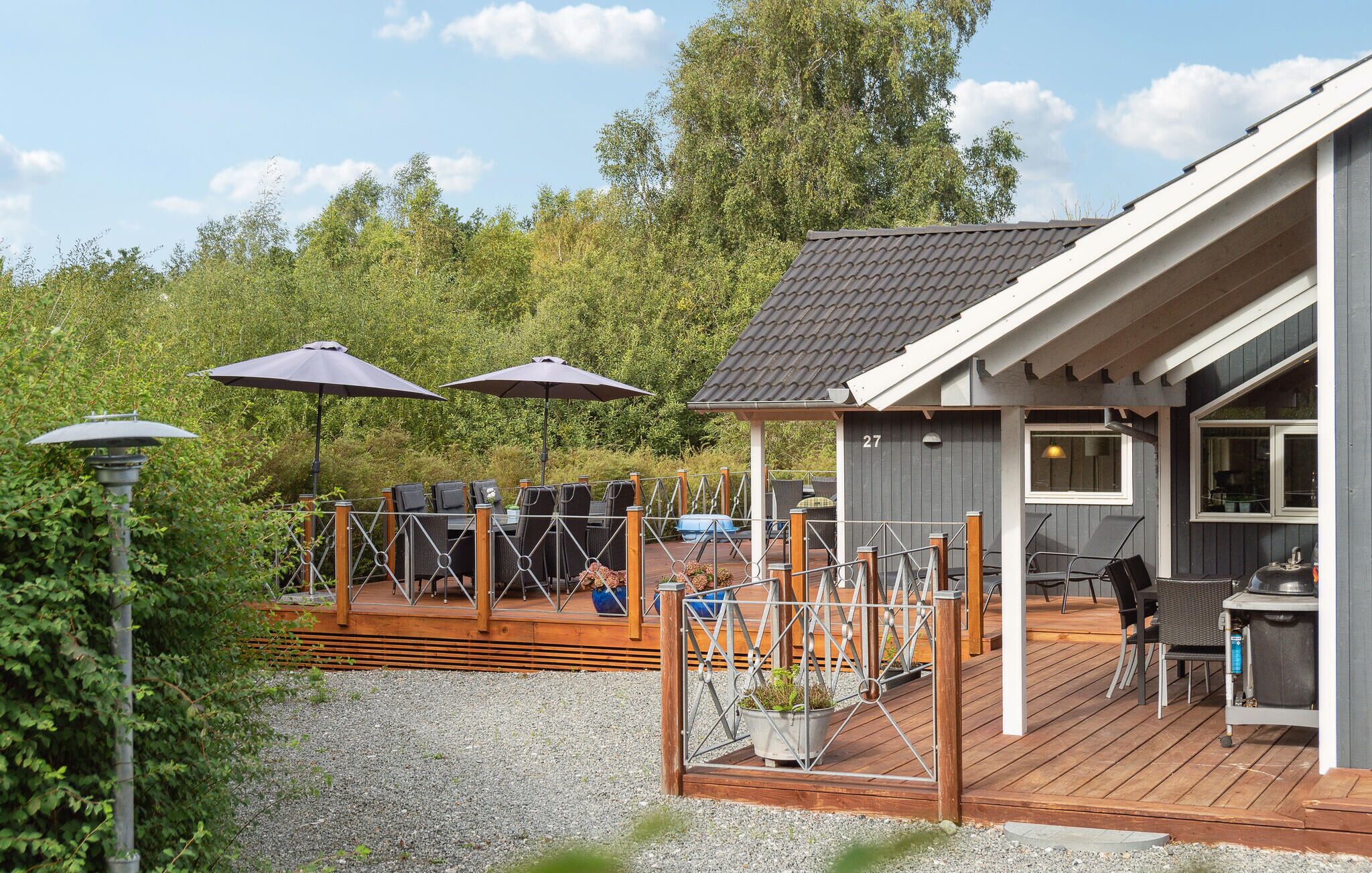 A wooden deck with outdoor seating, a small building with a number 27 sign, and a gravel area.