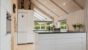 Une cuisine moderne avec des meubles blancs, un grand îlot central et une vue sur la verdure environnante.