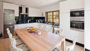 Una cocina moderna con armarios blancos, una mesa de comedor de madera y un ventanal grande.