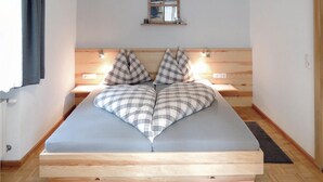 Una cama con un diseño de almohada a cuadros, cabecera de madera, mesitas de noche con lámparas y un pequeño marco de fotos sobre la cabecera.