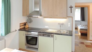 Cocina compacta con estufa, horno y lavavajillas, armarios de madera y ventana con cortinas.