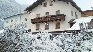 Un edificio de varios pisos con un balcón, rodeado de árboles y montañas cubiertas de nieve.
