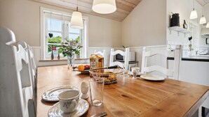 A wooden dining table with a white chair, a vase with flowers, a fruit bowl, and a bottle of apple cider juice.