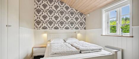Ein Schlafzimmer mit einem Bett, einem Fenster mit Blick auf Grünflächen und einer Wand mit Muster-Tapete.