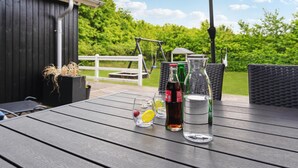 A wooden deck with a table set for drinks, a swing set, and a garden in the background.