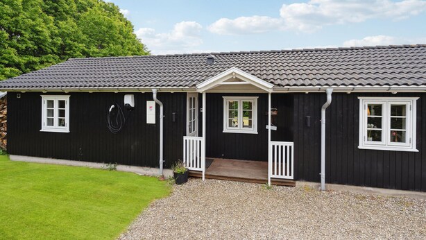 A black building with a tiled roof, a porch with a white railing, and a gravel driveway.