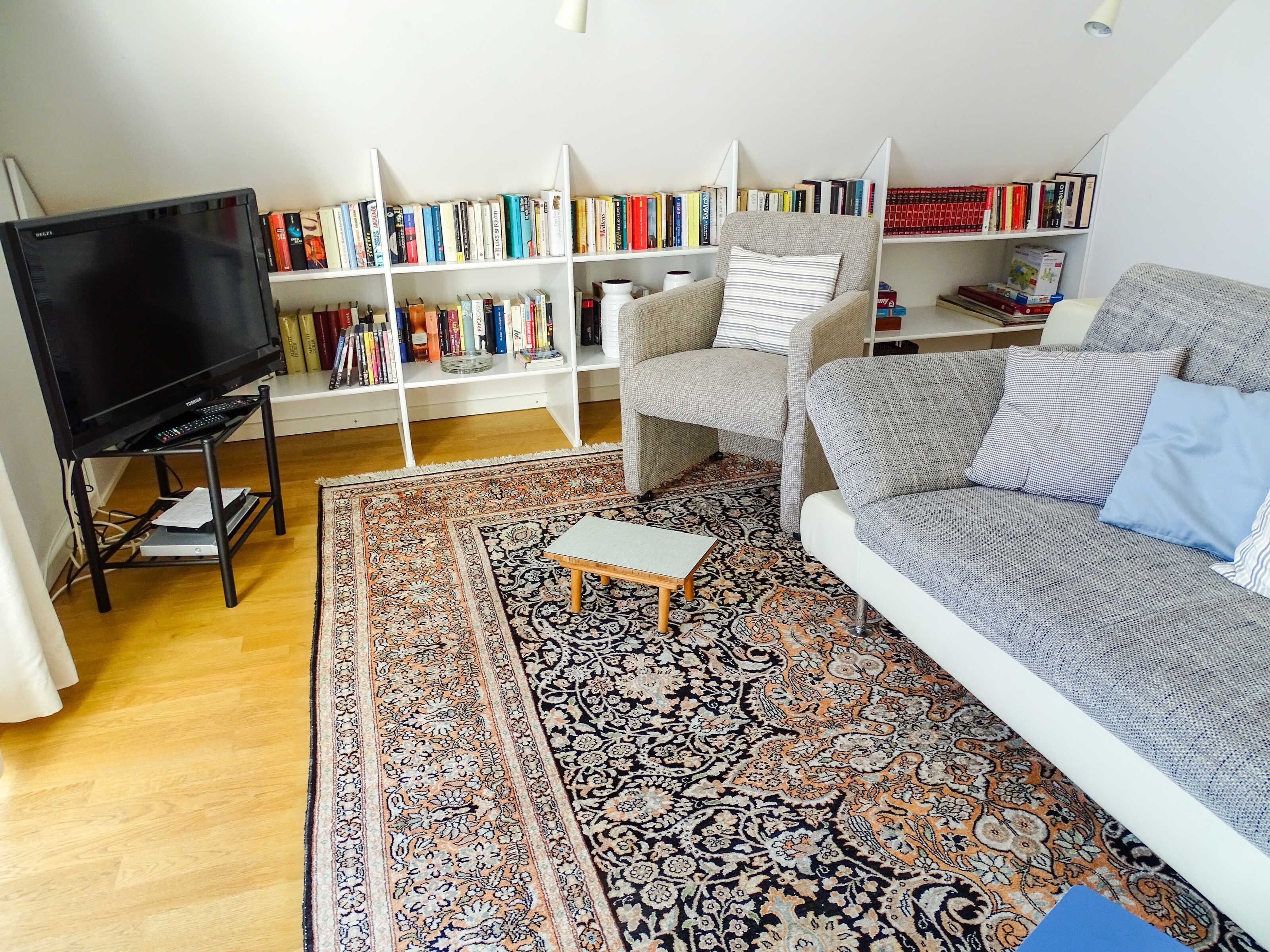 Un salon comprenant un canapé, une table basse, un téléviseur posé sur un meuble et une bibliothèque remplie de livres.