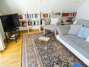 A living room with a sofa, a coffee table, a TV on a stand, and a bookshelf filled with books.