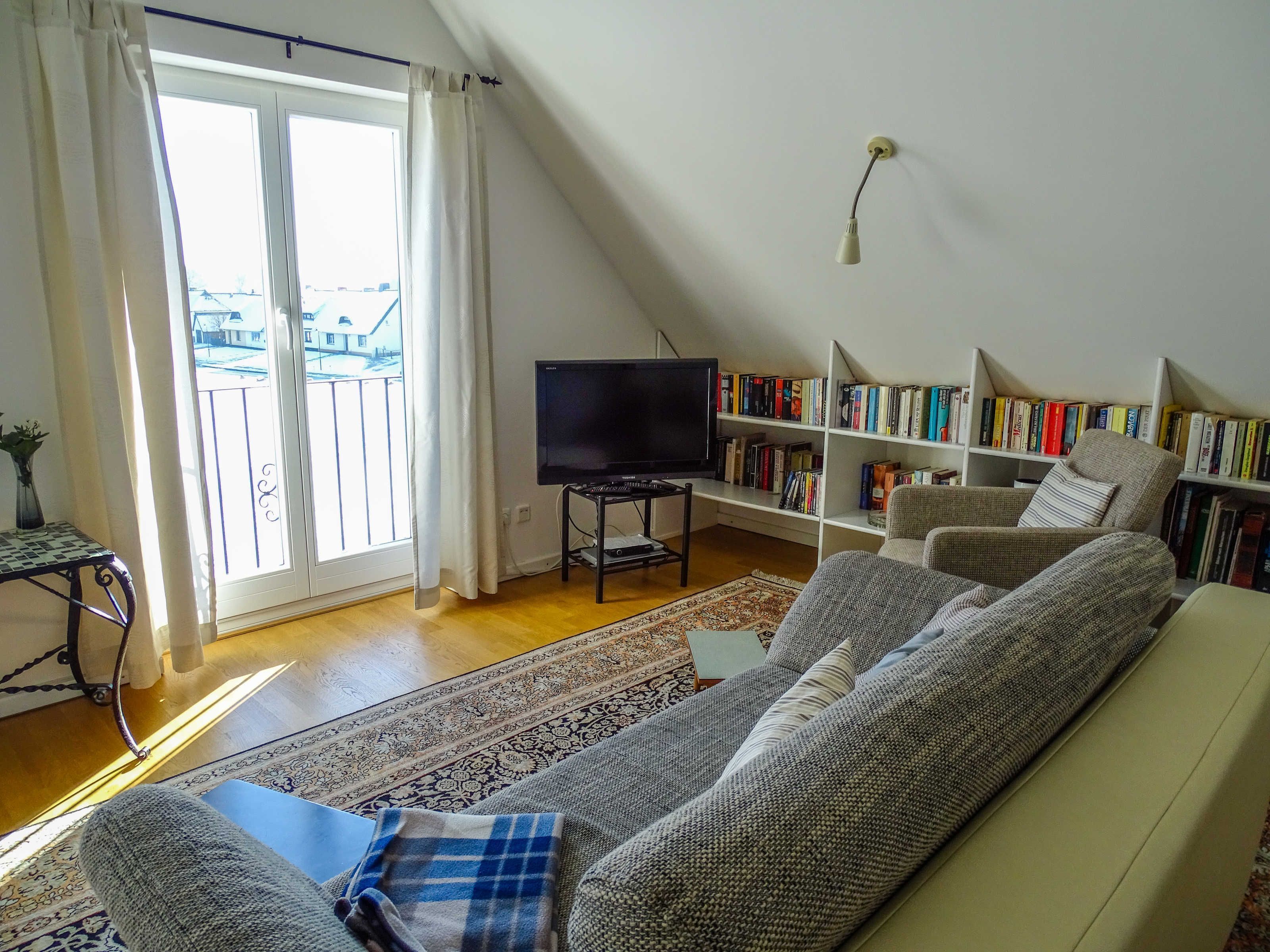 Ein Wohnzimmer mit Sofa, Fernseher, Bücherregal und Blick durch eine Schiebetür.