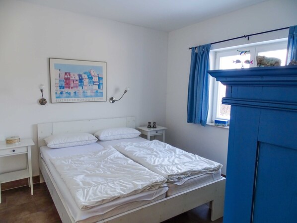 A bedroom with a bed, a nightstand, a bedside table, a window with curtains, and a wall-mounted picture.