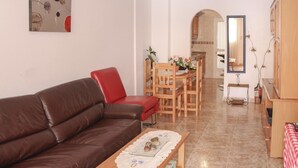 A living room with a brown leather sofa, a red chair, a wooden dining table with chairs, a small table with decorative items, and a mirror on the wall.