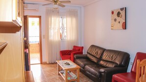A living room with a brown leather sofa, a wooden coffee table with a Monopoly game, a red chair, and a ceiling fan.