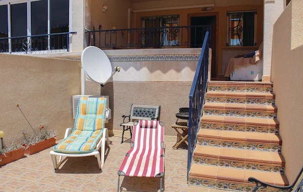 A sunlit outdoor seating area with two lounge chairs, a small table, and a staircase leading to an upper level.