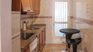 A compact kitchen with wooden cabinets, a granite countertop, a stainless steel sink, and a black bar stool.
