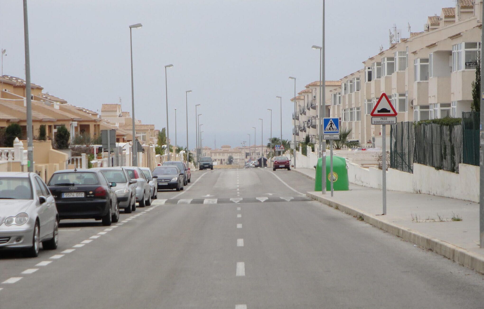 A street lined with parked cars and residential buildings.