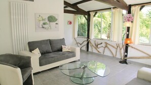 A living room with a grey sofa, a glass coffee table, and a lamp. There are windows with curtains and a view of greenery outside. - Amazing home in Rioux (Rioux)