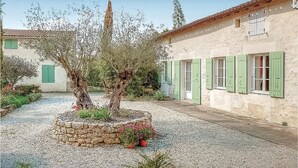 A courtyard with a stone planter, olive trees, and a building with green shutters. - Amazing home in Rioux (Rioux)