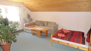 A cozy room with a wooden ceiling, a sofa, a small wooden table, and a bed with a red blanket.