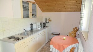 A compact kitchen with a sink, stove, and cabinets. There's a table with a tablecloth and a chair.