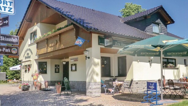 A traditional Alpine-style building with a balcony, outdoor seating area, and signs indicating nearby attractions.