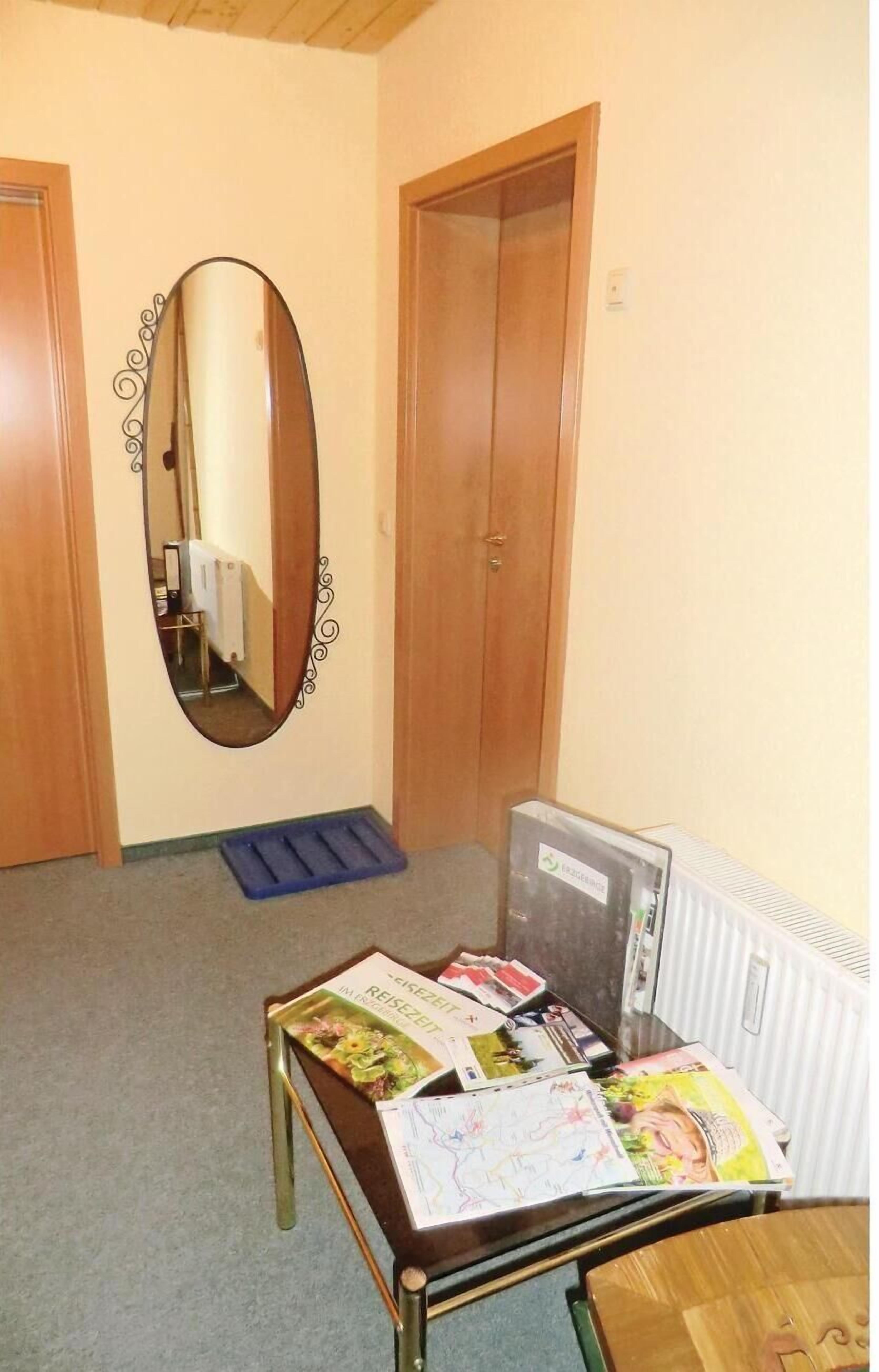 Een kamer met een houten deur, een spiegel met decoratieve lijst, een radiator en een tafel met tijdschriften en een dienblad.