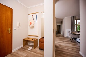 Habitación de hotel con puerta de madera, un banco pequeño de madera, un par de zapatos, una maleta y un perchero de pared.