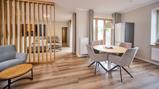 A modern living room with a wooden partition, a grey sofa, a wooden coffee table, and a dining area with a round table and chairs. - Residence Seestern Whg S-21 .. - See-21 (Kühlungsborn)