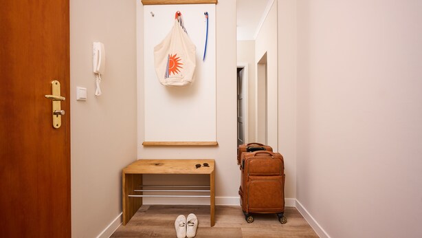 A hotel room with a wooden bench, a coat rack with a bag and a phone, a suitcase, and a pair of shoes on the floor. - Residence Seestern Whg S-21 .. - See-21 (Kühlungsborn)