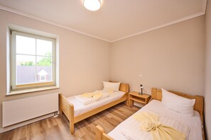 Une chambre avec deux lits simples, une fenêtre, une table de chevet avec une lampe et un radiateur.
