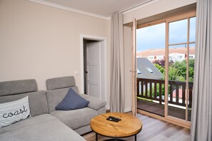 Un salon moderne avec un canapé gris, une table basse ronde en bois et une porte-fenêtre coulissante donnant sur un balcon extérieur.