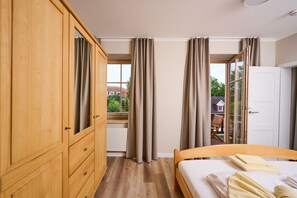 Un dormitorio con un armario de madera, una cama con ropa blanca y vistas a una casa a través de amplios ventanales.