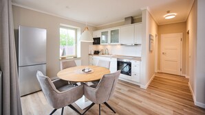 A modern kitchen with white cabinets, a built-in oven, and a dining area with a round table and two chairs. - Residence Seestern Whg S-21 .. - See-21 (Kühlungsborn)