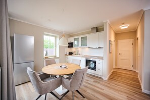Een moderne keuken met witte kastjes, een inbouwoven en een eethoek met een ronde tafel en twee stoelen.