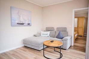 Een woonkamer met een bank, een salontafel en een schilderij van zeilboten.