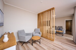 Una habitación de hotel moderna con suelo de madera, dos sillones grises, una pequeña mesa de madera y un separador de madera.