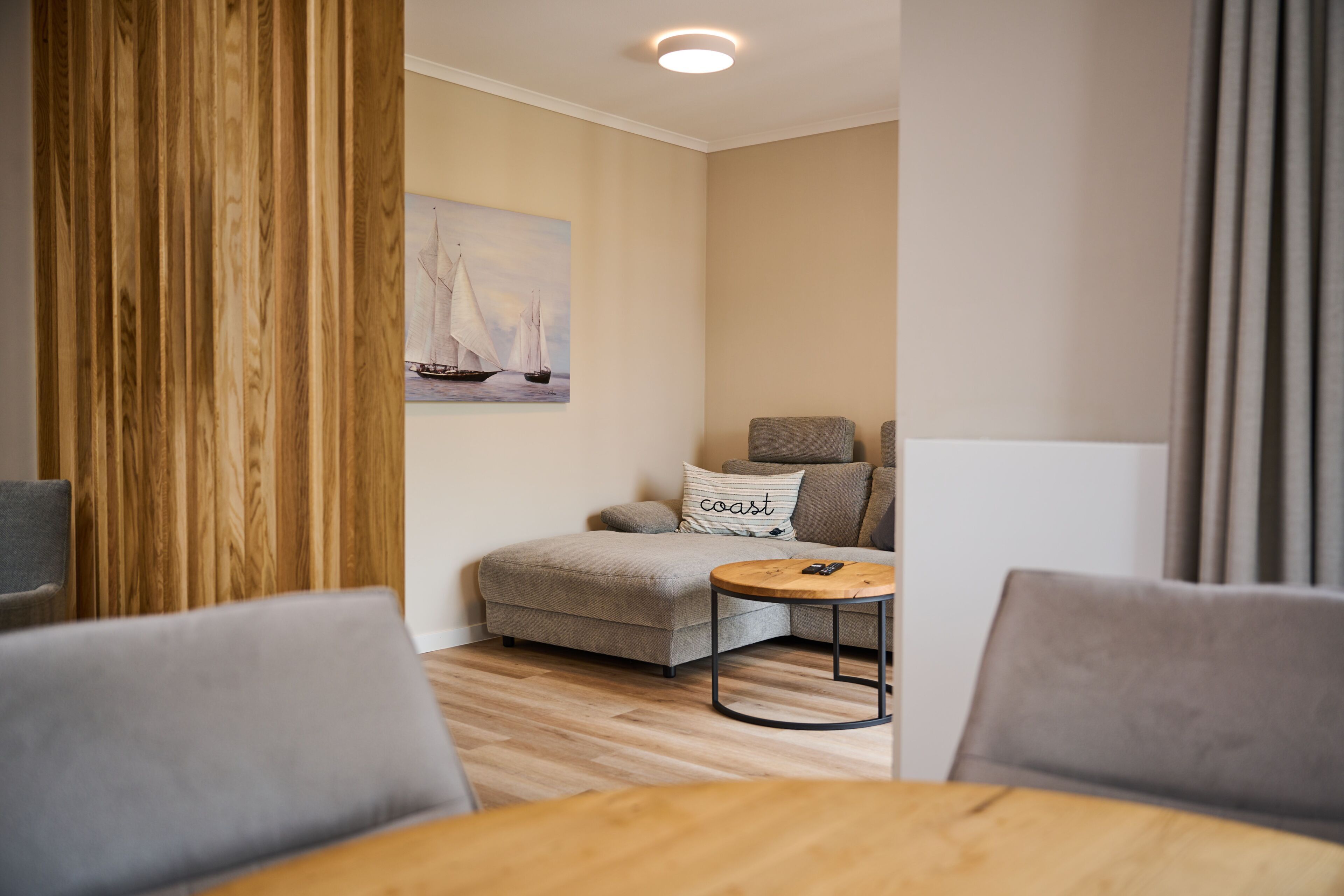 A modern living room with a sofa, a coffee table, and a painting of sailboats on the wall.