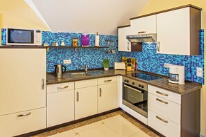 Une cuisine de taille réduite avec des meubles blancs, un four à micro-ondes, une cuisinière et un évier.