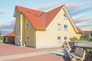 En gul bygning med rødt tag, mange vinduer og et anlagt indgangsparti med en statue og bænk.