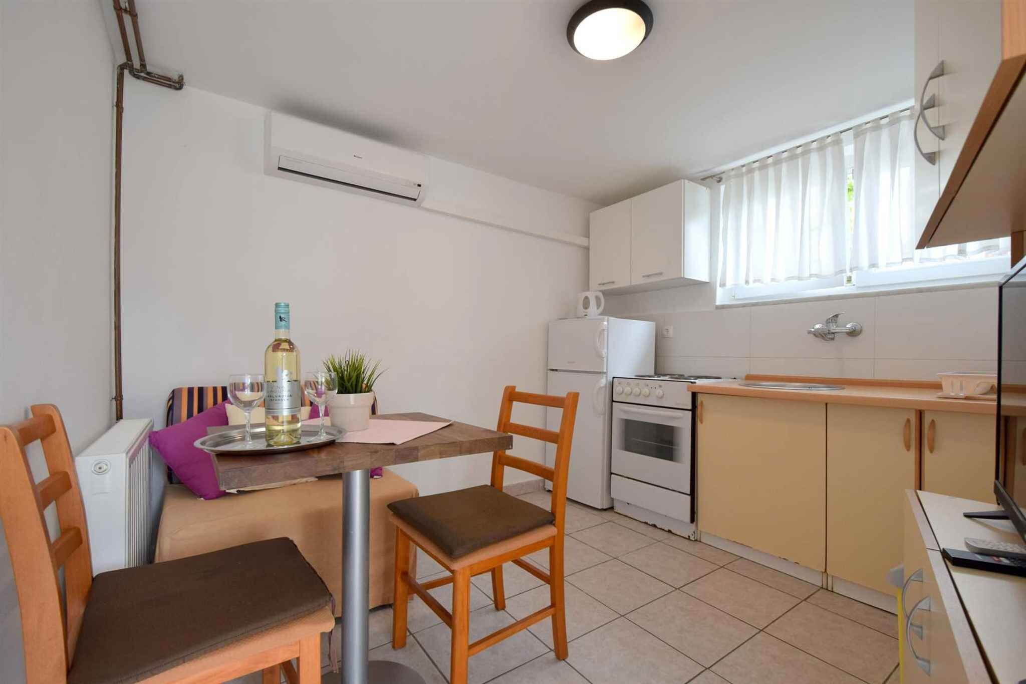 Una cuina compacta amb zona de menjador, incloent taula, cadires, nevera, forn i finestra amb cortines.