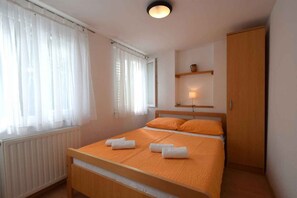 A bedroom with a bed, a radiator, a wooden wardrobe, and a shelf with a lamp.