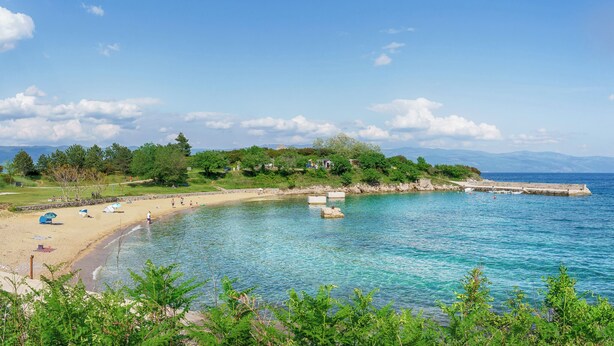 A beach with clear blue water, a sandy shore, and a stone pier extending into the sea. - Holiday apartment mit Terrasse (Čižići)