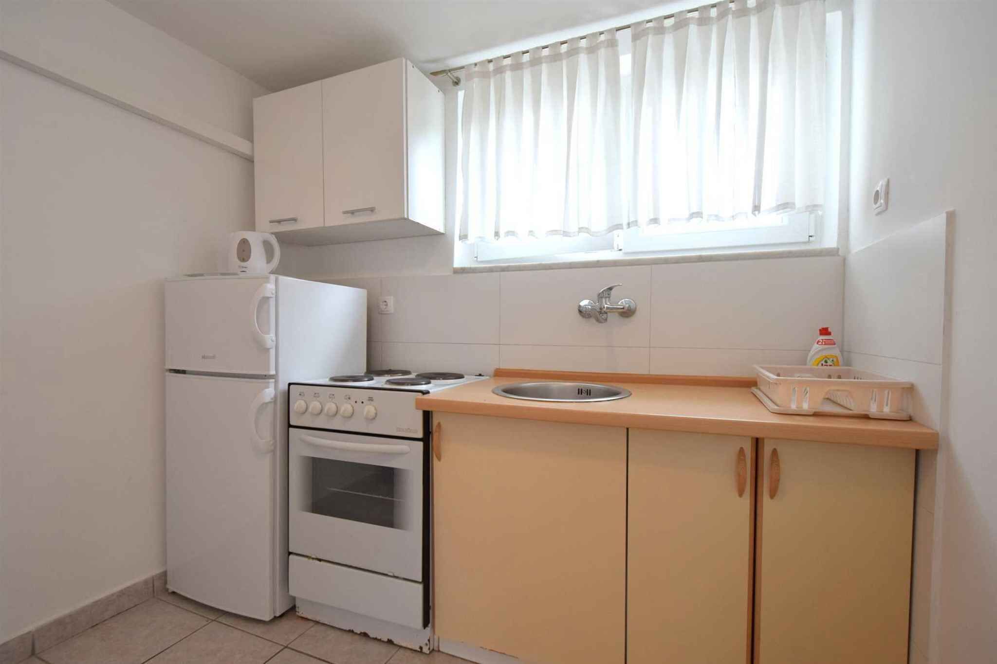 A compact kitchen with a refrigerator, stove, oven, and a window with curtains.